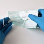 two hands with blue gloves holding a surgical mask
