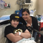 A woman with brown hair is hugging her son, who is in a hospital bed.
