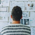 man wearing black and white stripe shirt looking at white printer papers on the wall