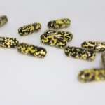 Eleven capsules filled with yellow and black particles.